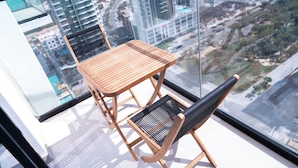 A balcony with a wooden table and two chairs, a glass wall, and a city view. - Free Housekeeping Visits During Your Stay - Stayshort - 1 Bed in Jumeirah Village Circle for 4 in a Great Location (Dubai)