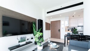 A modern living room with a flat-screen TV, a dining table set with plates and cutlery, a sofa, and a kitchen in the background. - Free Housekeeping Visits During Your Stay - Stayshort - 1 Bed in Jumeirah Village Circle for 4 in a Great Location (Dubai)