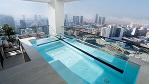 A rooftop infinity pool with a city view, modern furniture, and a glass railing. - Free Housekeeping Visits During Your Stay - Stayshort - 1 Bed in Jumeirah Village Circle for 4 in a Great Location (Dubai)