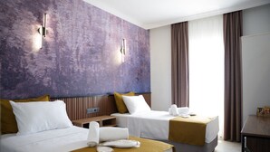 Habitación de hotel con dos camas, una mesita de noche de madera, un escritorio y un ventanal con cortinas.