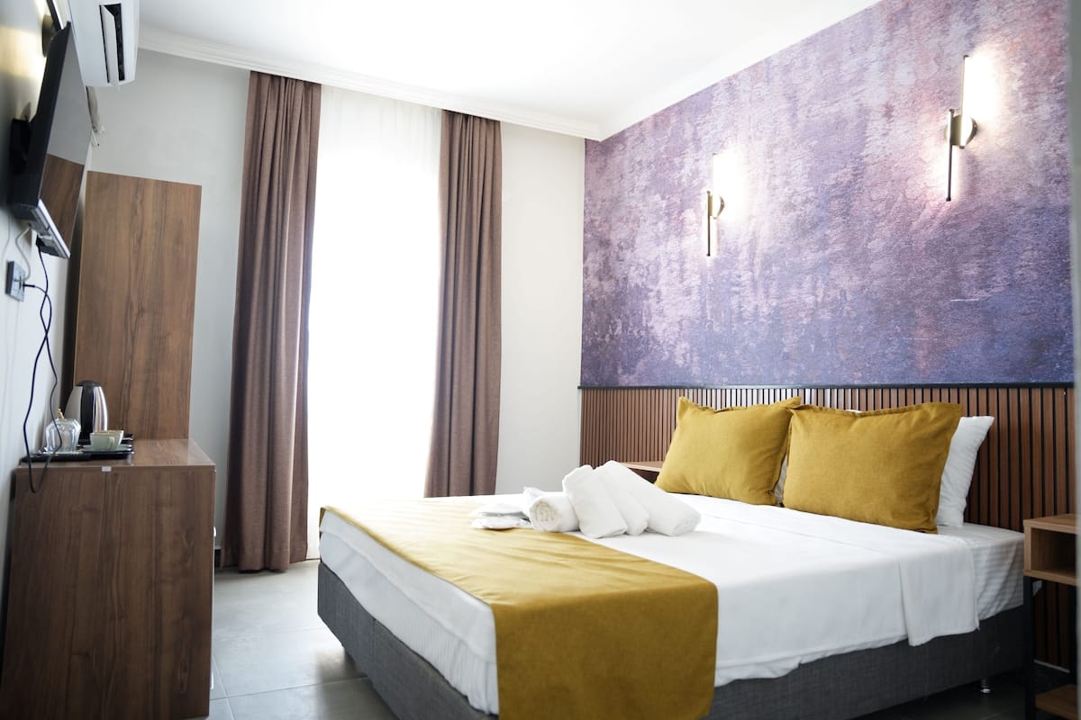 Una habitación de hotel moderna con una cama grande, un escritorio de madera y un televisor montado en la pared.