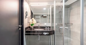 Un baño moderno con cabina de ducha de vidrio, lavamanos con encimera negra y un florero con flores blancas.