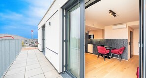 Um edifício moderno com porta de vidro que dá para uma área de refeições com duas cadeiras vermelhas e uma mesa.