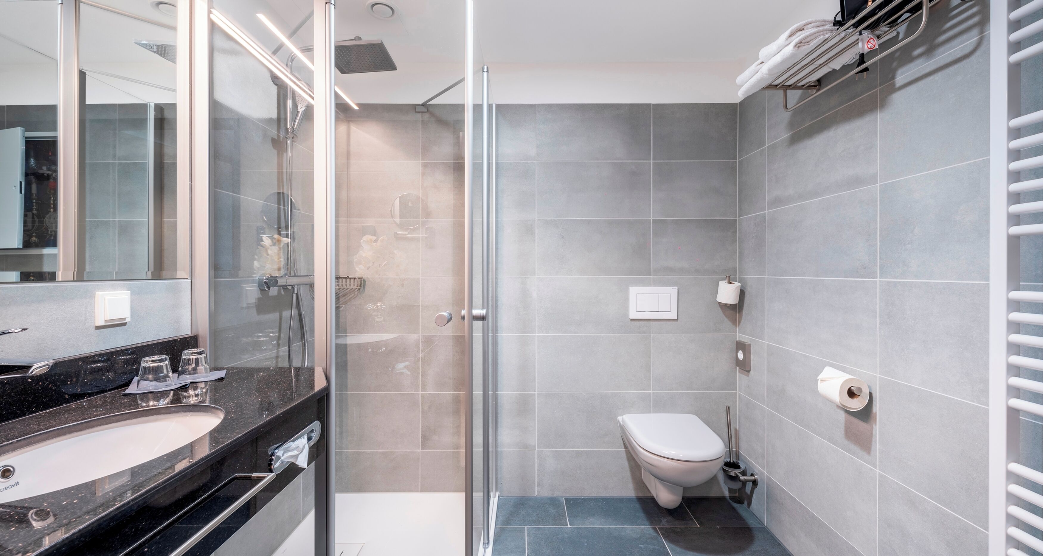A modern bathroom with a glass shower enclosure, a white toilet, and a black countertop with a sink.