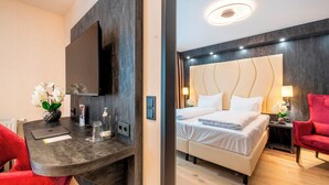 A modern hotel room with a bed, a desk, a red chair, and a TV mounted on the wall. - PLAZA Residence Wiener Neustadt (Wiener Neustadt)
