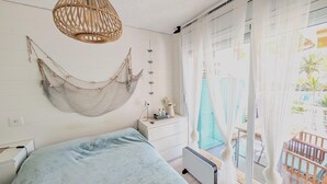 A bedroom with a hammock, a bed, a bedside table, a radiator, and a view of the outdoors. - Apartment 'Sea and Charm' with Shared Pool, Wi-Fi, and Air Conditioning (Miami Platja)