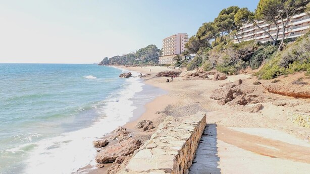 A coastal beach with a stone wall, sandy beach, and buildings in the background. - Apartment 'Sea and Charm' with Shared Pool, Wi-Fi, and Air Conditioning (Miami Platja)