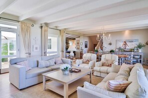 A spacious living room with a light-colored sofa, armchairs, and a coffee table. There is a dining area with a table and chairs in the background. - Sea of Dreams | Langbaai Beach | Spectacular Sea View (Hermanus)