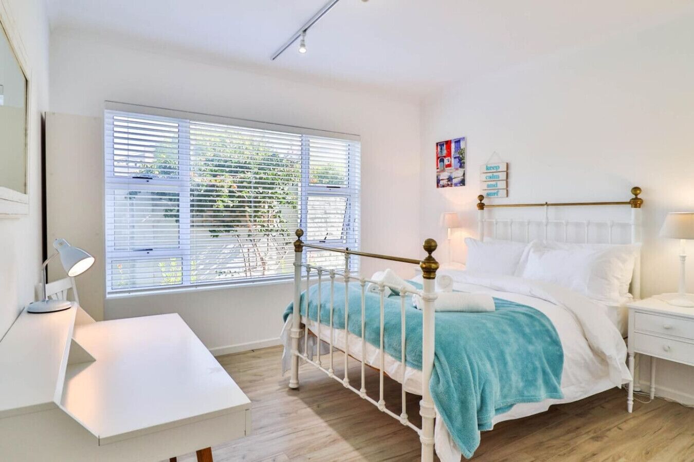 Een slaapkamer met een wit bed, een bureau en een raam met jaloezieën.
