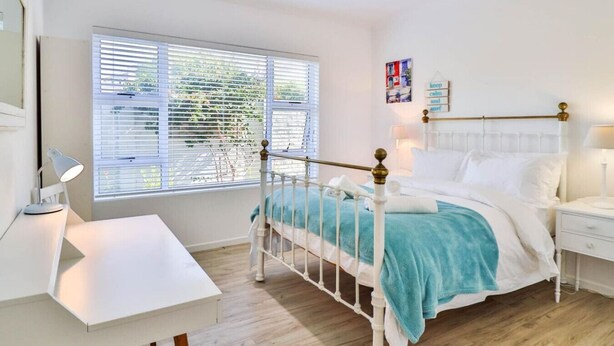 A bedroom with a white bed, a desk, and a window with blinds. - Vonkelwyn | Bright and Breezy by Grotto Beach (Hermanus)