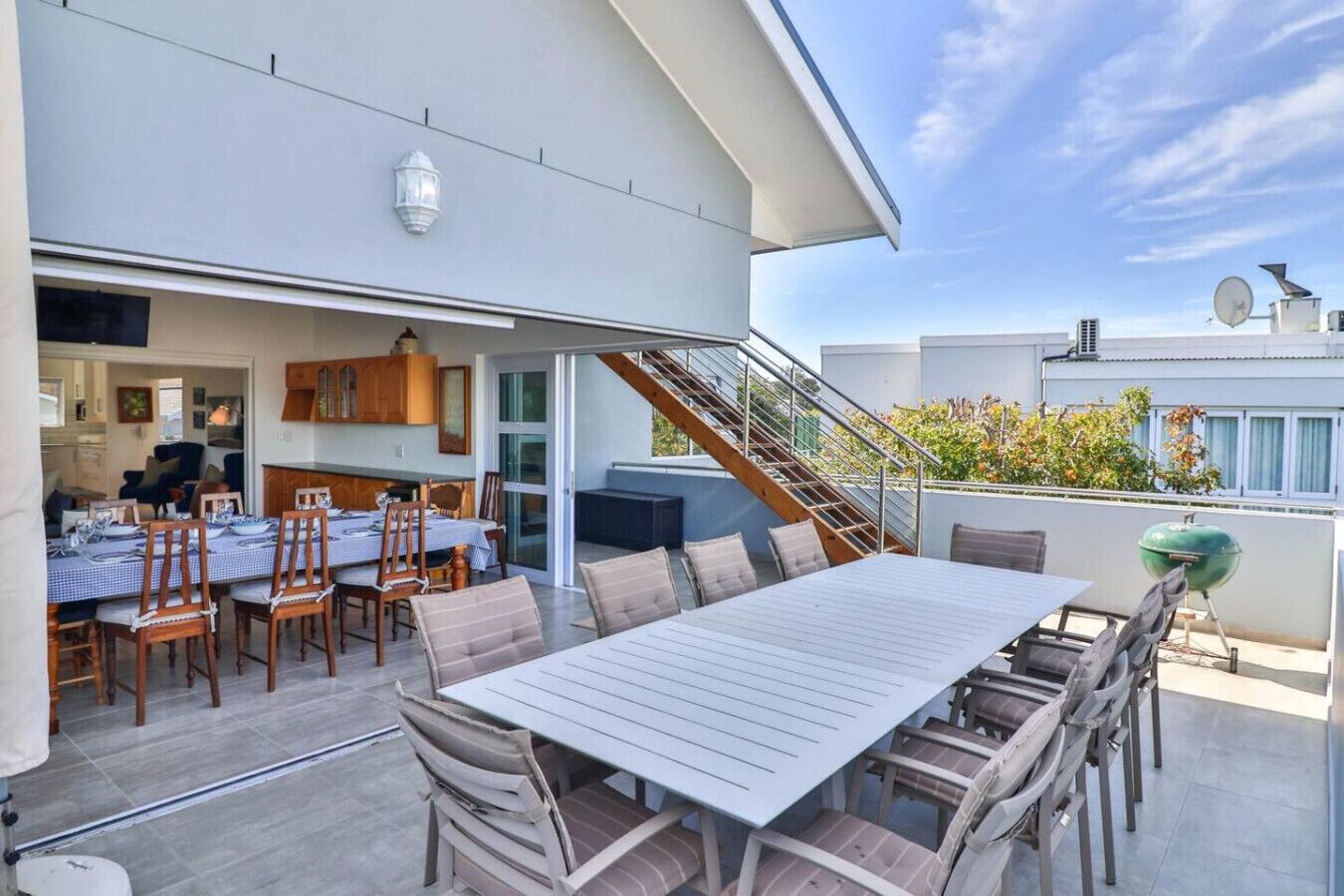 Une terrasse sur le toit, aménagée avec une table et des chaises, un barbecue et un escalier menant à un niveau supérieur.