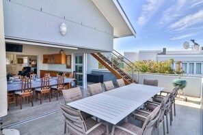 Une terrasse sur le toit, aménagée avec une table et des chaises, un barbecue et un escalier menant à un niveau supérieur.