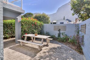 A patio area with a wooden table and benches, surrounded by a brick wall and various plants. - Vonkelwyn | Bright and Breezy by Grotto Beach (Hermanus)
