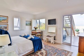 A bedroom with a bed, desk, TV, and a balcony with a view. - Vonkelwyn | Bright and Breezy by Grotto Beach (Hermanus)