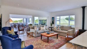 A spacious living room with a large sofa, a coffee table, and a dining area with chairs and a table. - Vonkelwyn | Bright and Breezy by Grotto Beach (Hermanus)