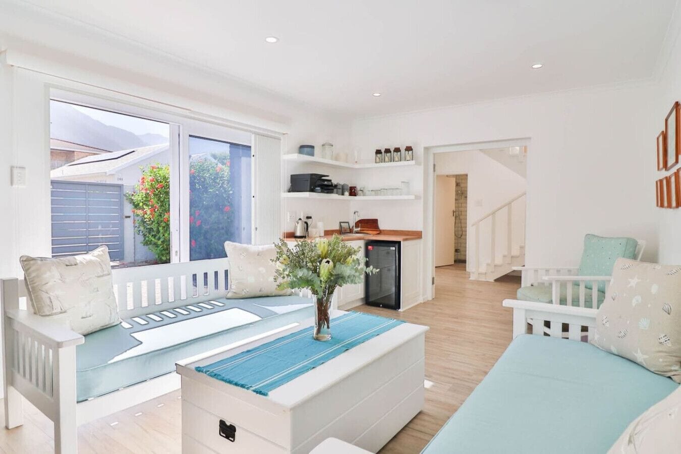 Uma sala de estar moderna com um sofá, uma mesa de centro e uma cozinha ao fundo.