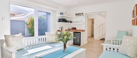 Uma sala de estar moderna com um sofá, uma mesa de centro e uma cozinha ao fundo.