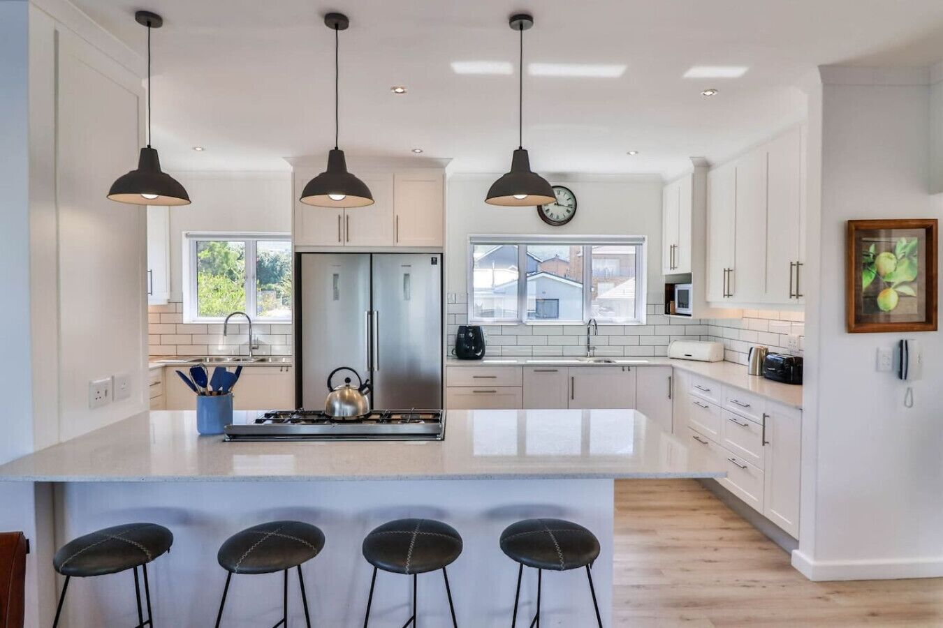 Une cuisine moderne dotée d’un îlot central, d’appareils électroménagers en acier inoxydable, de luminaires suspendus et d’une grande fenêtre.