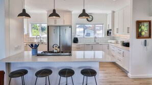 A modern kitchen with a central island, stainless steel appliances, pendant lighting, and a large window. - Vonkelwyn | Bright and Breezy by Grotto Beach (Hermanus)