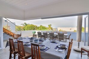 A dining area with a checkered tablecloth, wooden chairs, and a view of greenery and buildings. - Vonkelwyn | Bright and Breezy by Grotto Beach (Hermanus)