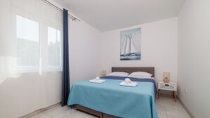 Ein Schlafzimmer mit Bett, Nachttisch, Lampe, einem Gemälde und einem Fenster mit Vorhängen.