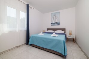 A bedroom with a bed, a nightstand, a lamp, a painting, and a window with curtains. - Modern apartment for 4-5 persons with terrace, sea view (Dramalj)