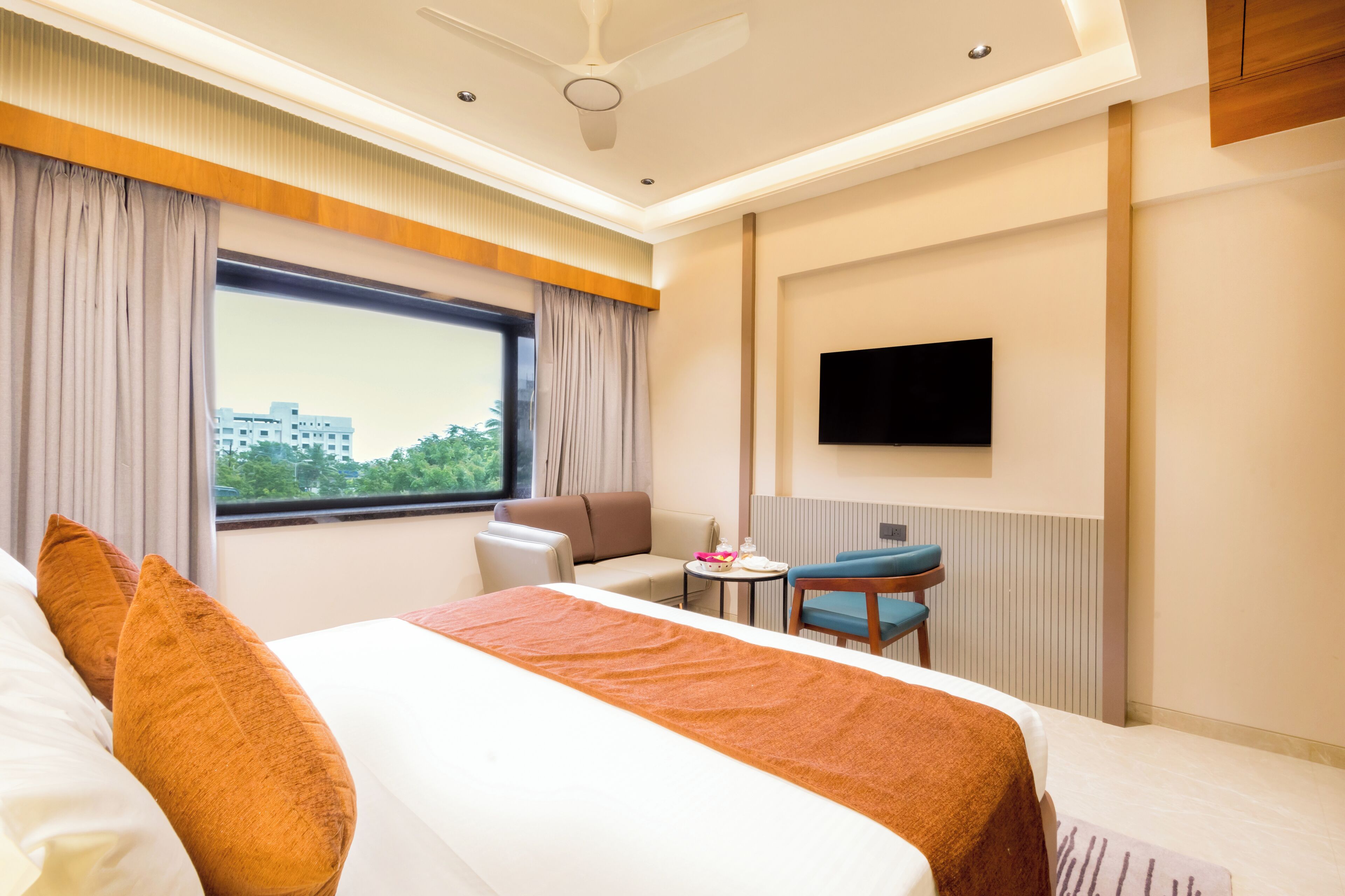 A hotel room with a bed, a desk, a chair, a TV, and a window with a view of buildings.