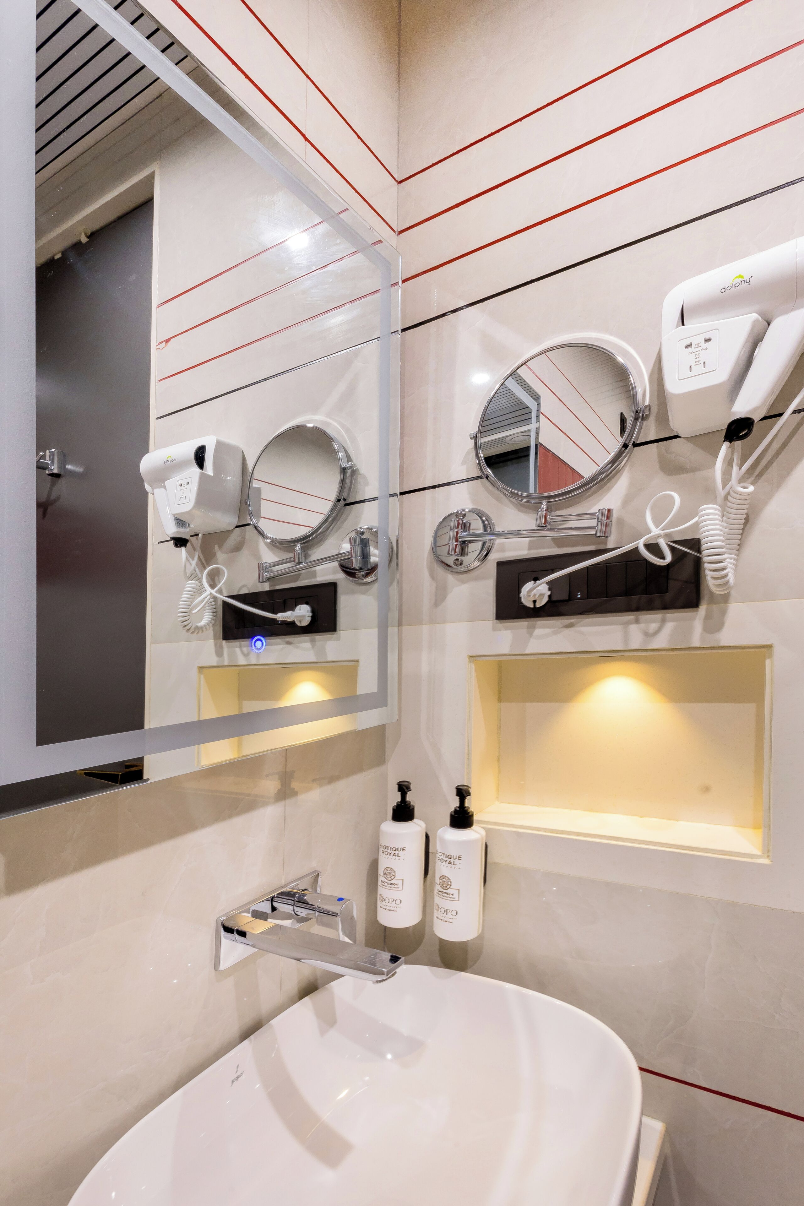 A modern bathroom with a large mirror, two hair dryers, a sink, and a vanity with toiletries.