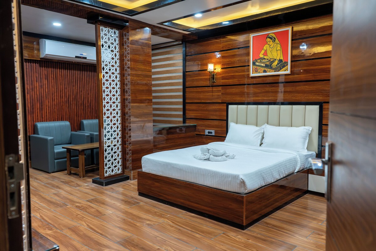 Habitación de hotel con piso de madera, cama con ropa blanca, sofá azul y un panel decorativo en la pared.