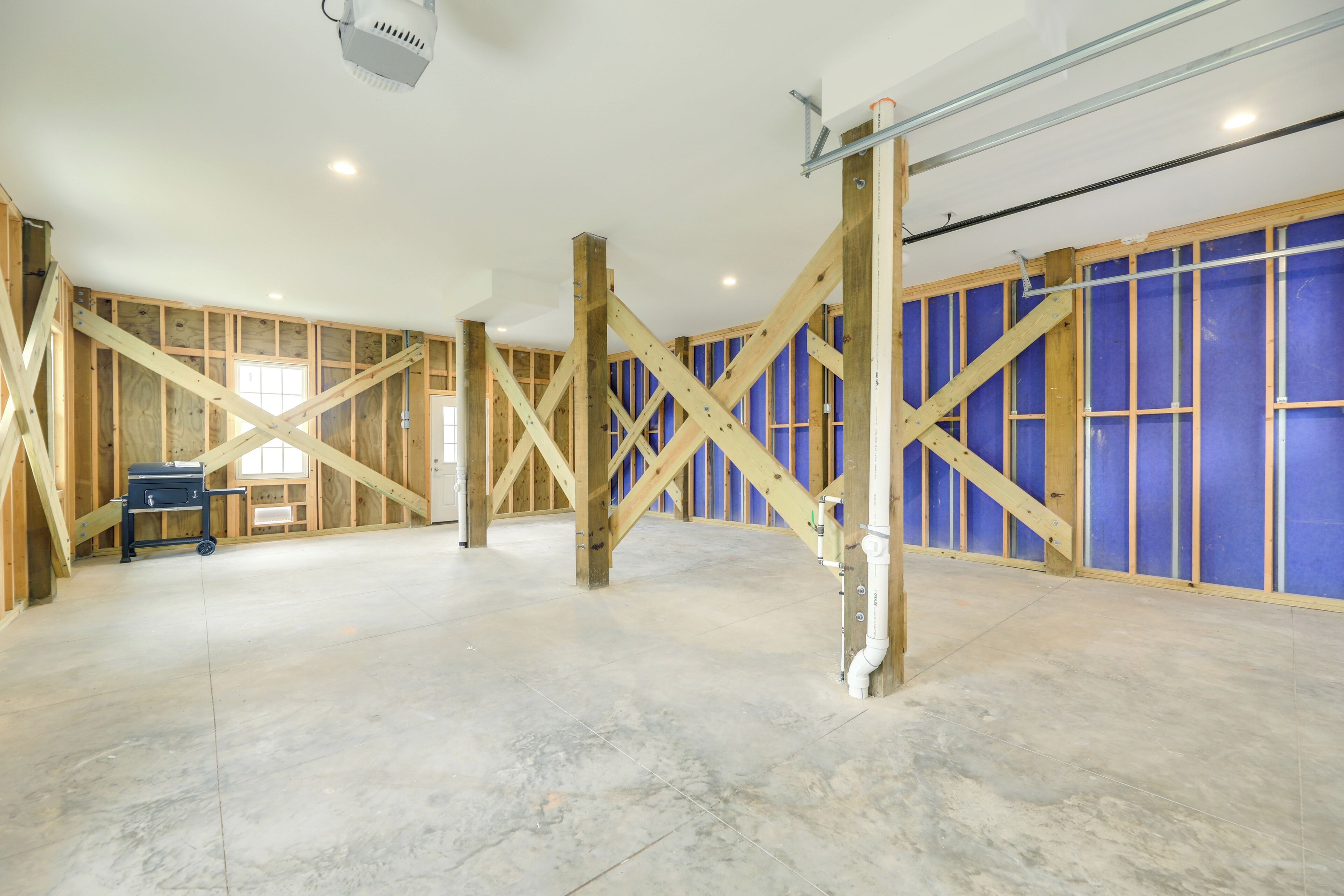 A spacious room with exposed wooden beams, a tiled floor, and a blue wall with insulation.