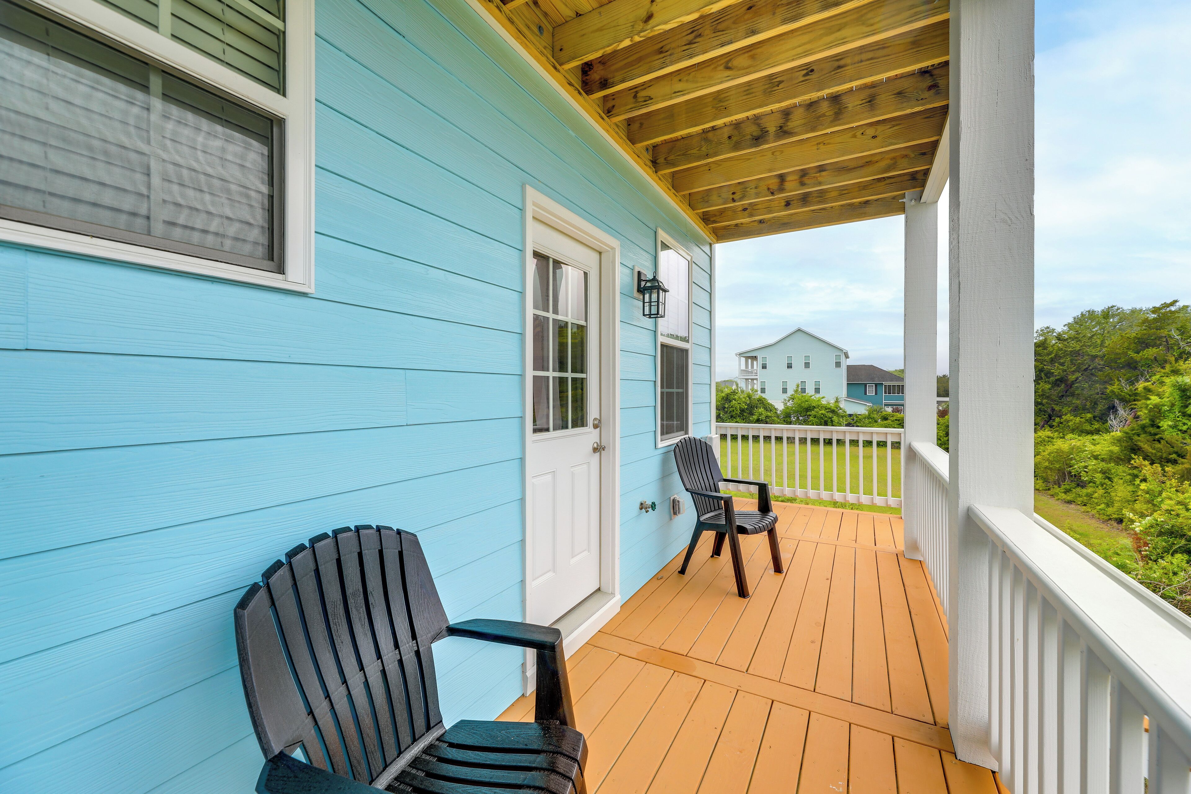 A porch with two Adirondack chairs, a wooden ceiling, and a white railing.