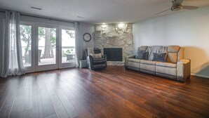 A living room with a stone fireplace, a sofa, a leather chair, and a ceiling fan. - Water-view Patio, Near Golf! Port Duncan Retreat (Afton)