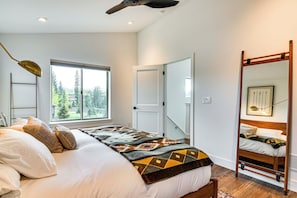 Une chambre à coucher avec un lit, une fenêtre donnant sur des arbres, un ventilateur de plafond et un miroir.