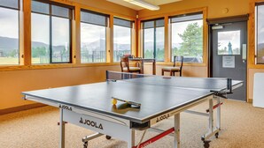 A ping pong table in a room with large windows, a door with a sign, and a view of mountains. - Luxury WP Mtn Cabin, Free Shuttle, Views & Garage (Fraser)