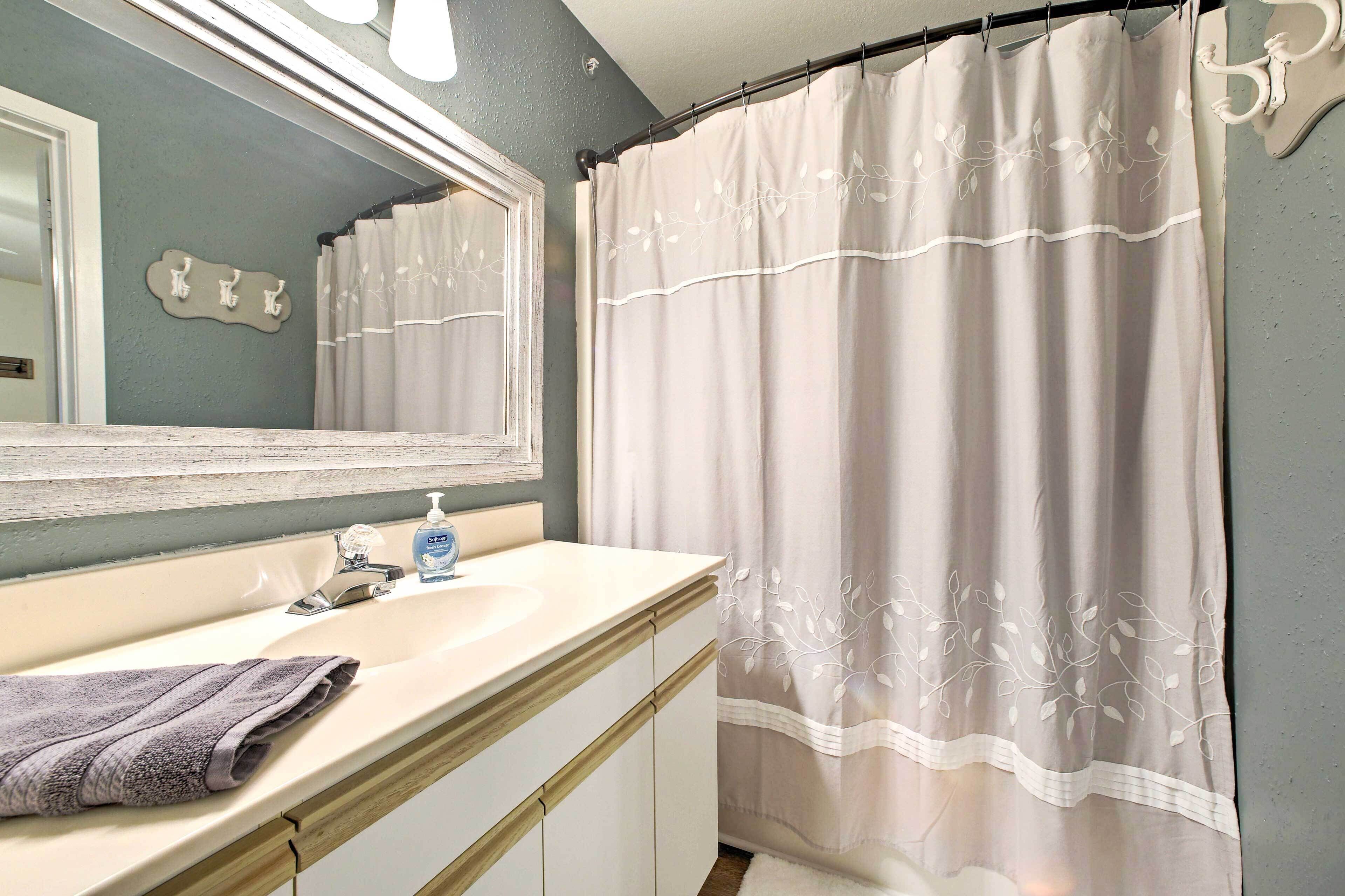 A bathroom with a white sink, mirror, and a shower curtain with a leaf pattern.