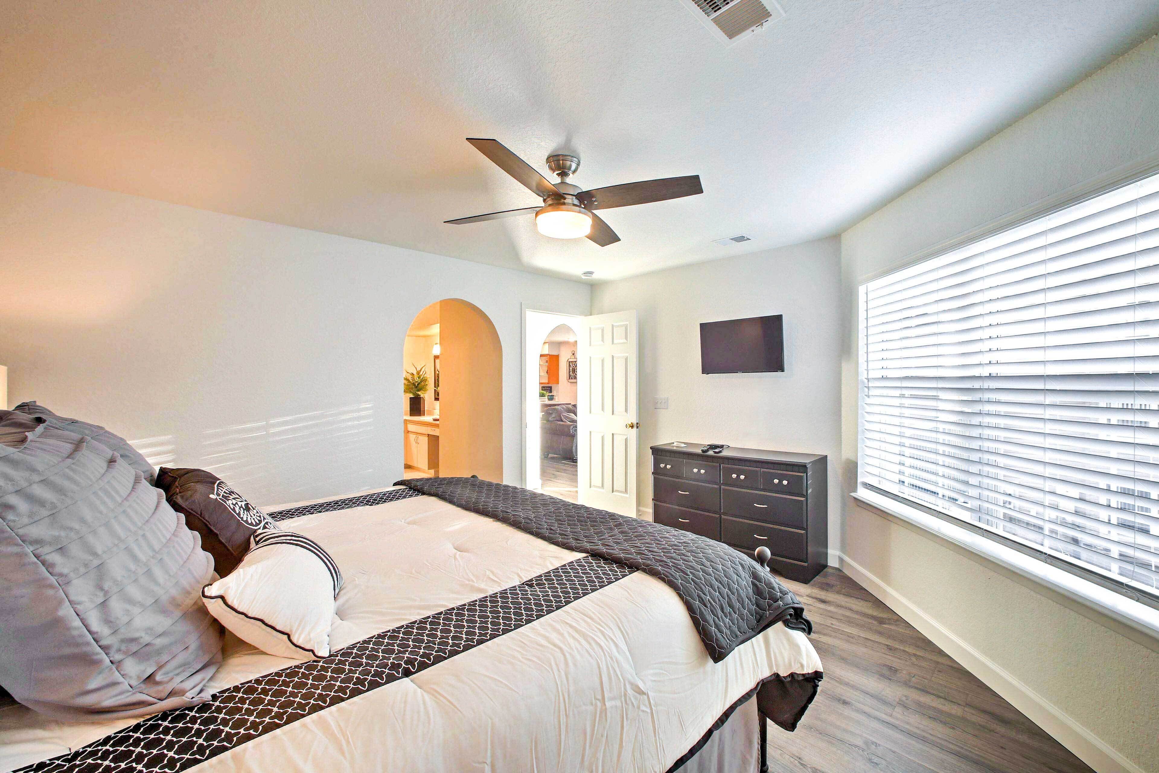 A bedroom with a bed, a ceiling fan, a dresser, and a window with blinds.