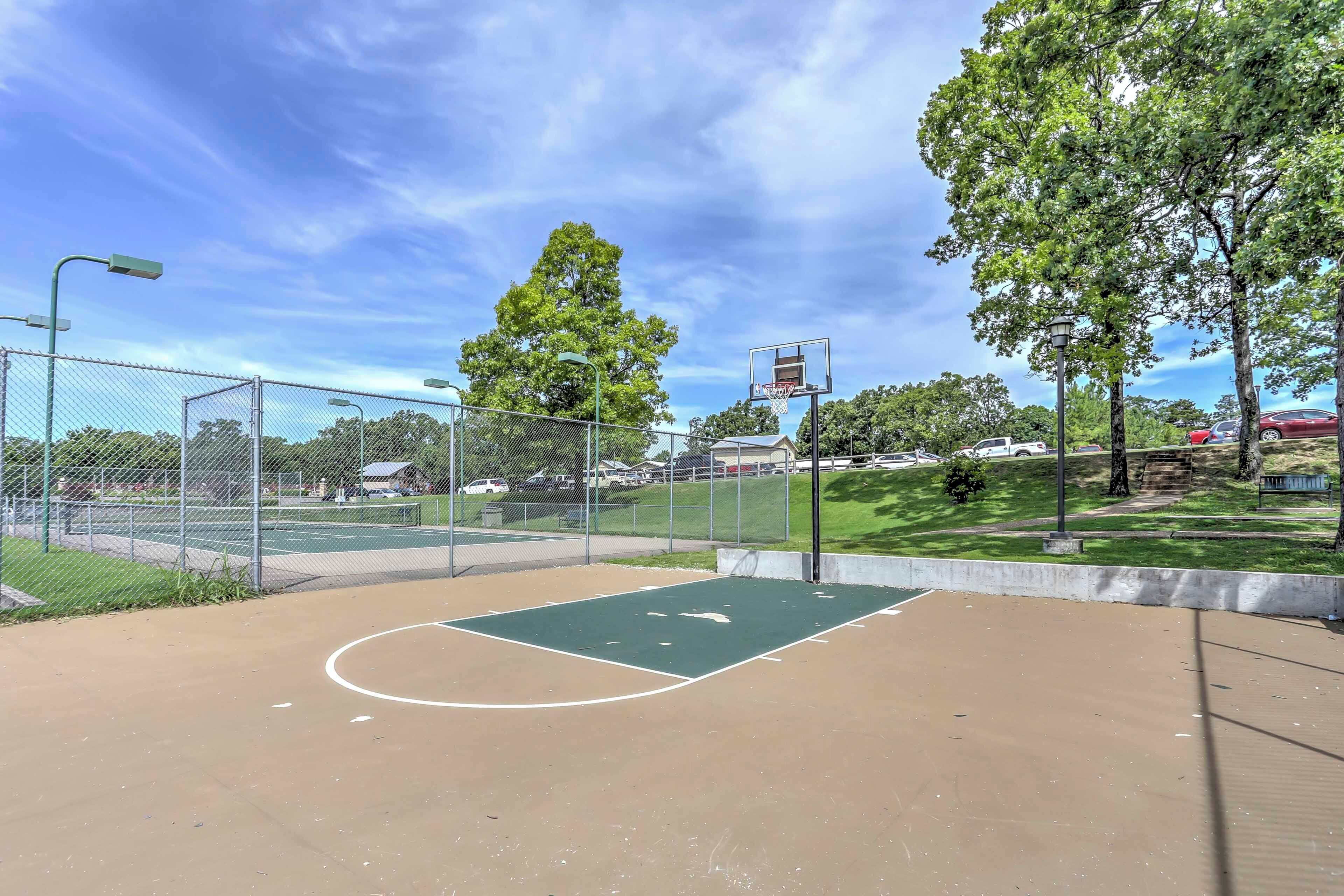 An outdoor basketball court with a chain-link fence, basketball hoop, and trees in the background.