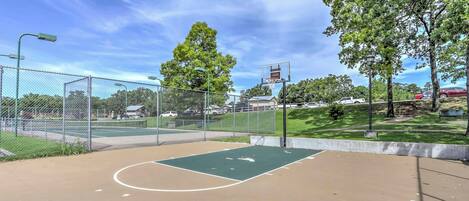 An outdoor basketball court with a chain-link fence, basketball hoop, and trees in the background.