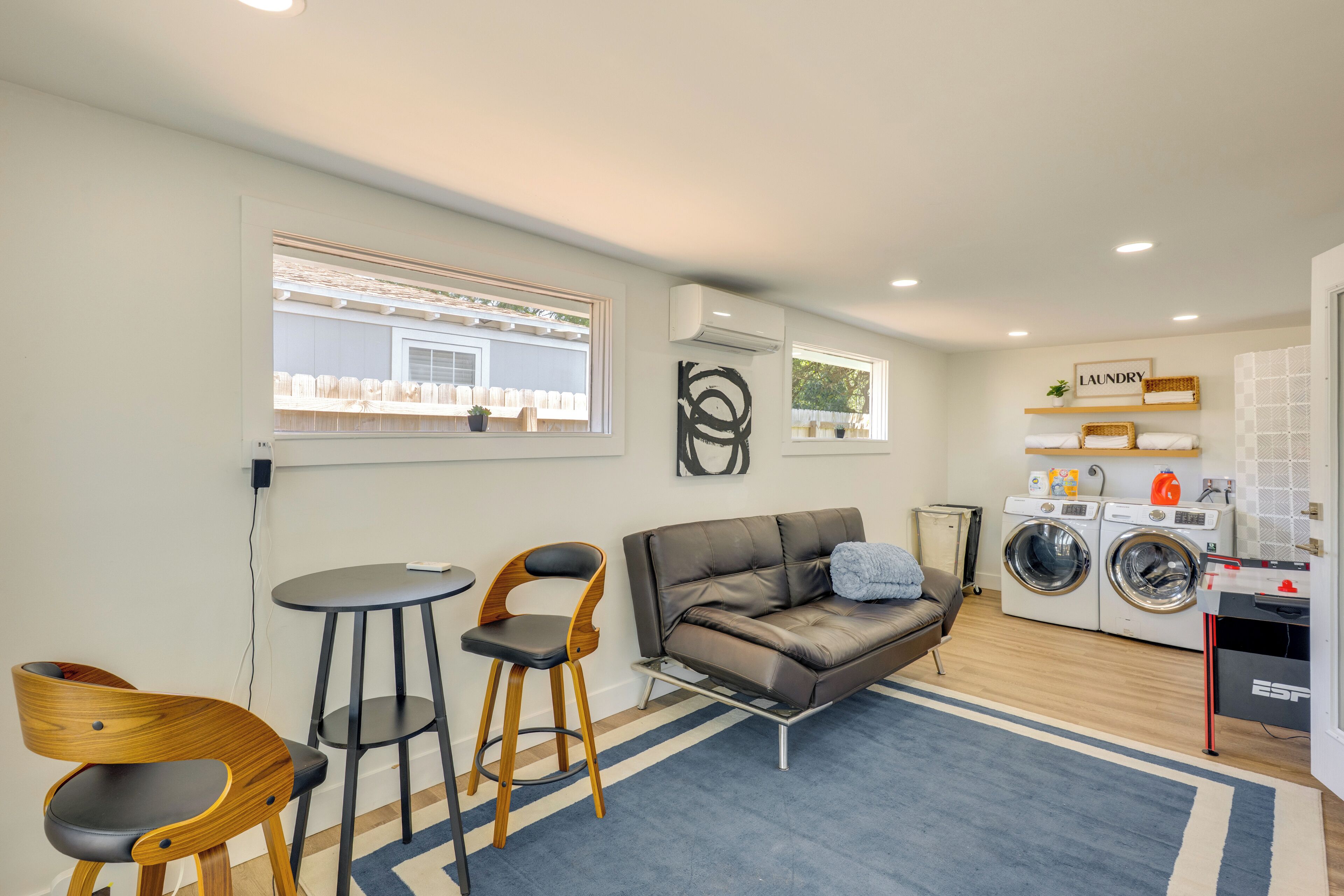 Un salon moderne avec un canapé, deux fauteuils en bois, une petite table ronde et un lave-linge.