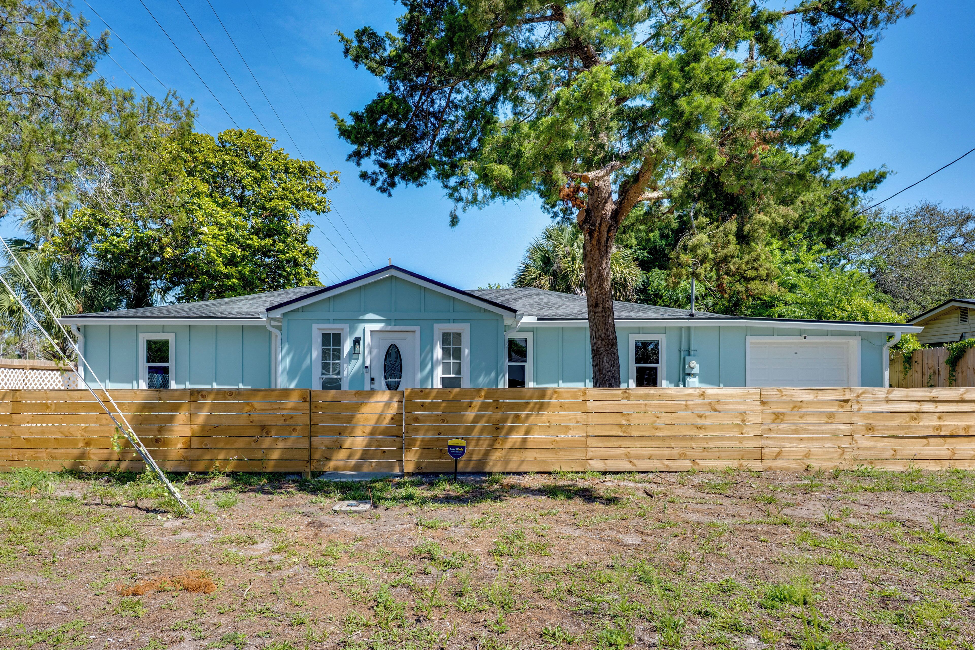 A single-story house with a garage, a wooden fence, and a large tree in front.