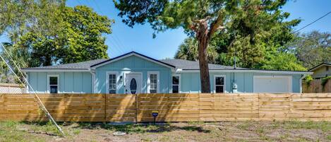 A single-story house with a garage, a wooden fence, and a large tree in front.