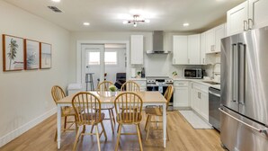 Una cocina moderna con armarios blancos, un refrigerador de acero inoxidable, sillas de madera y una mesa de comedor.