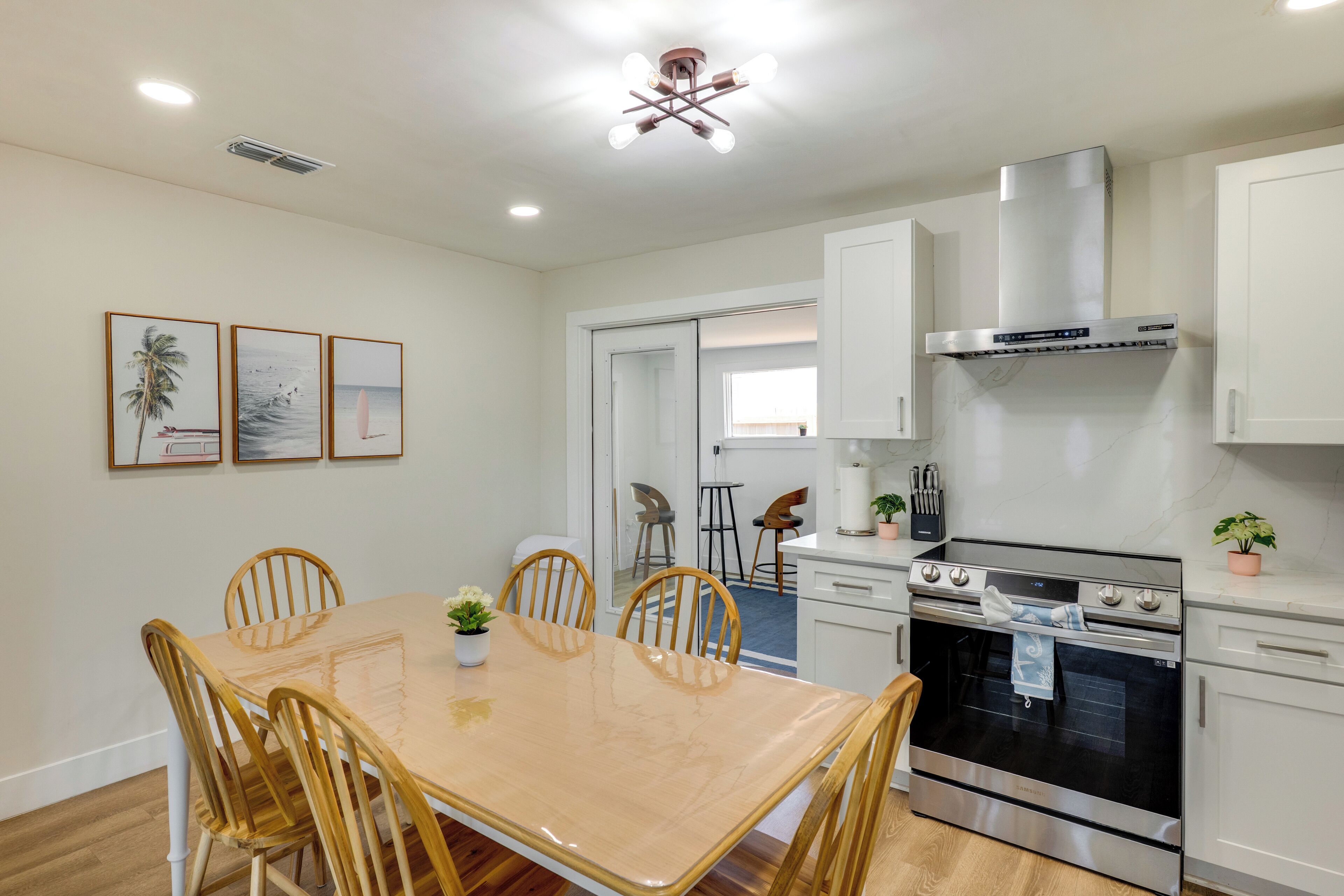 A modern kitchen with white cabinets, a stainless steel oven, and a dining table with wooden chairs.
