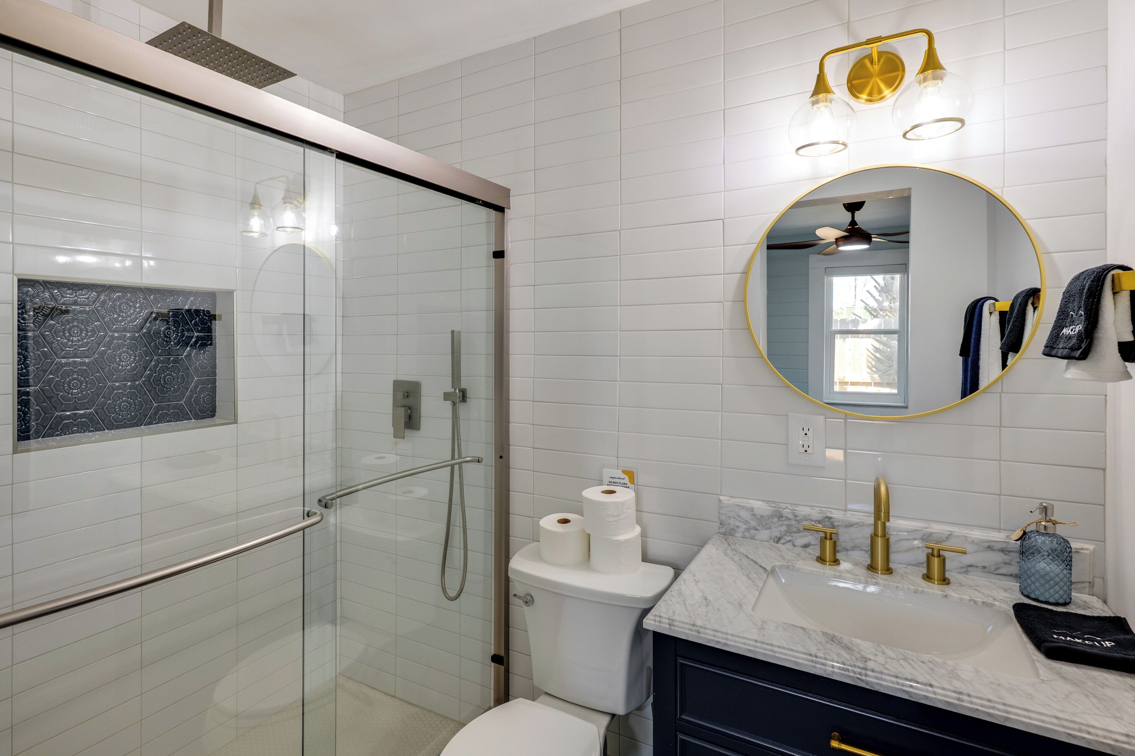 A modern bathroom with a glass-enclosed shower, a marble sink, and a round mirror.
