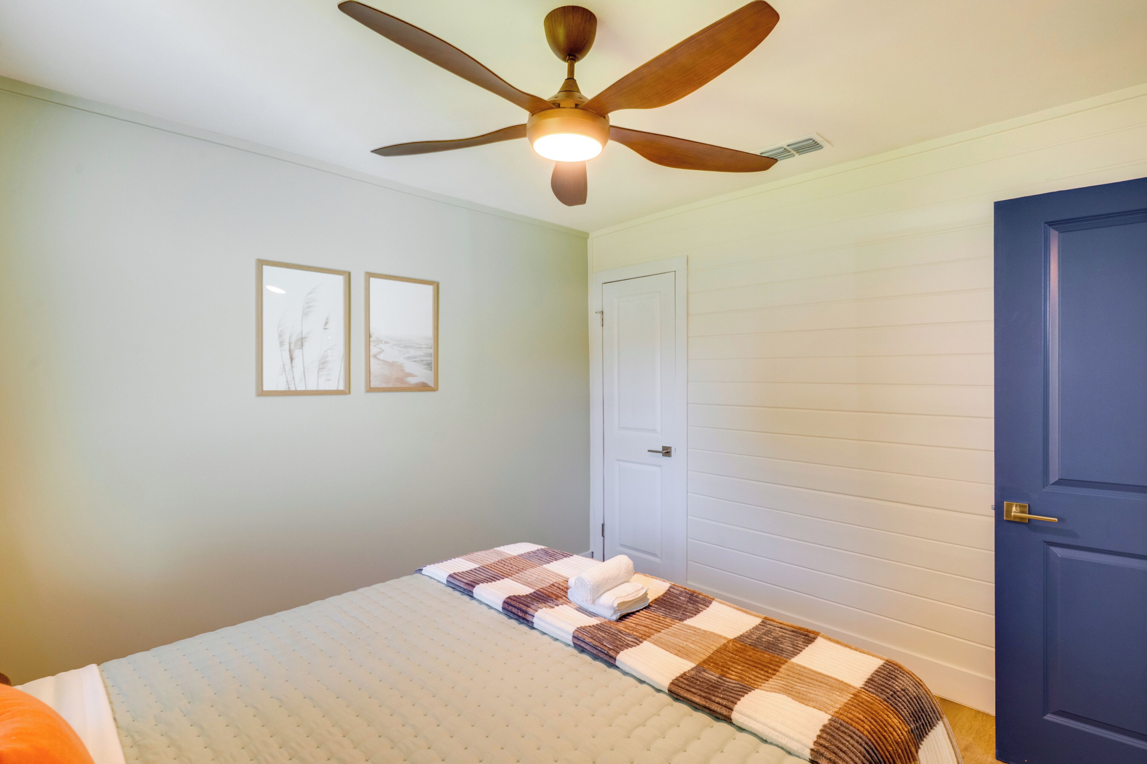 Une chambre à coucher avec un lit, un ventilateur de plafond, une porte et deux tableaux encadrés accrochés au mur.