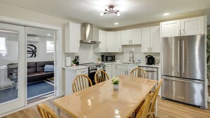 Una cocina moderna con armarios blancos, un refrigerador de acero inoxidable y una zona de comedor con una mesa y sillas de madera.
