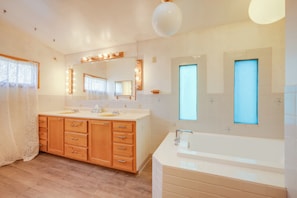 Ein geräumiges Badezimmer mit einem großen Waschtisch, einer Badewanne und zwei Fenstern.