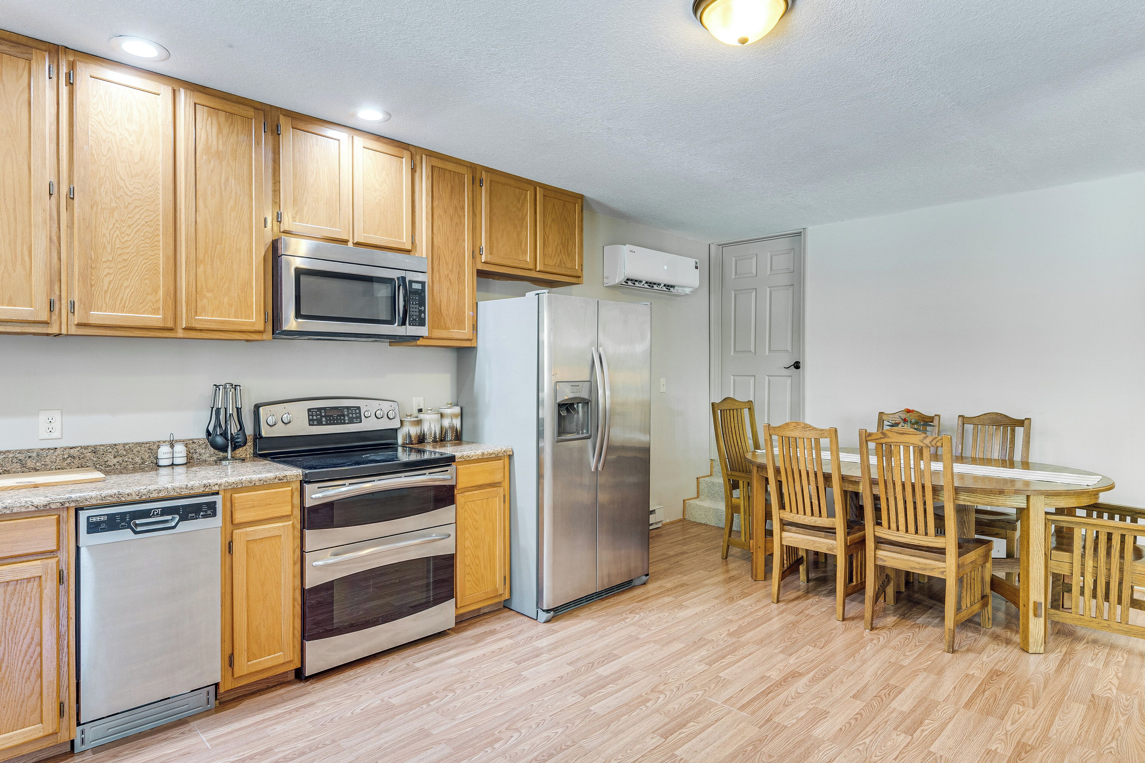 A kitchen with wooden cabinets, stainless steel appliances, and a dining area with wooden chairs.