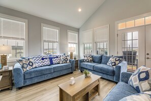 A living room with two blue sofas, a wooden coffee table, and a view through large windows.