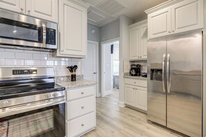 A modern kitchen with stainless steel appliances, white cabinetry, and a light wood floor.